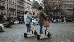 Deux personnes circulant en trottinettes électriques sur une place pavée en France.