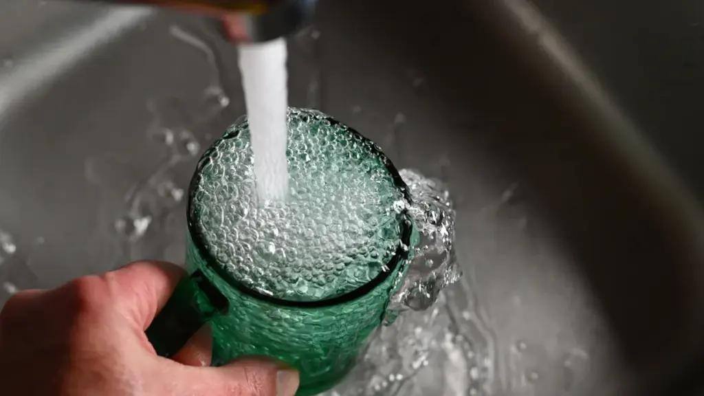 Main d'une personne remplissant un verre d'eau sous un robinet de cuisine.