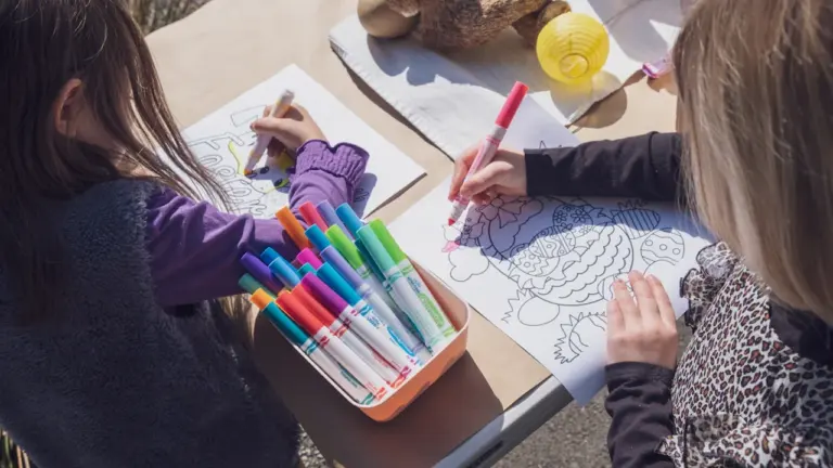 Deux jeunes filles utilisant des feutres pour colorier sur une table en extérieur.