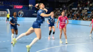 Joueuse de handball en plein saut s'apprêtant à tirer au but durant un match intense.