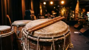 Deux baguettes en bois posées sur une peau de tambour tendue sur scène sombre.