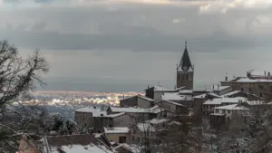 Vue panoramique hivernale sur une commune française avec clocher sous un ciel nuageux.