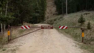 Barrière fermée barrant l'accès à un chemin forestier en terre battue.