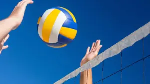 Mains de joueurs de volley-ball s'étendant vers un ballon jaune et bleu en plein ciel.