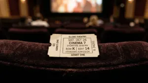 Un billet de cinéma posé sur un fauteuil sombre devant une salle de projection floue.