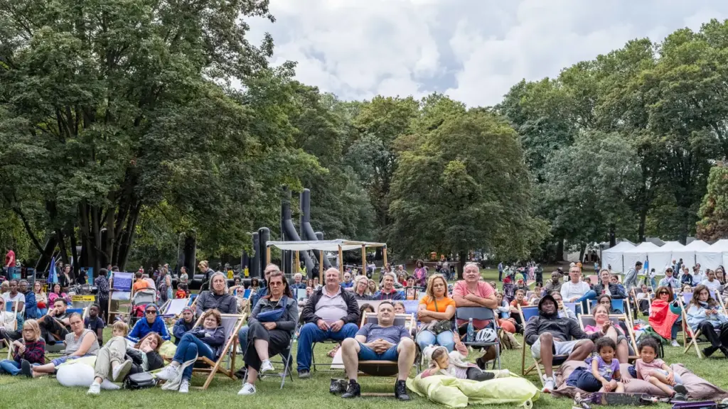 Un public diversifié assis sur des chaises longues dans un parc verdoyant et arboré.