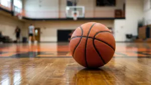Un ballon de basket orange est posé sur le parquet brillant d'un gymnase intérieur.