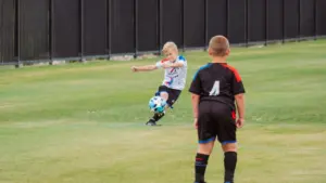 Deux jeunes garçons jouent au football sur un terrain en herbe verte en journée.