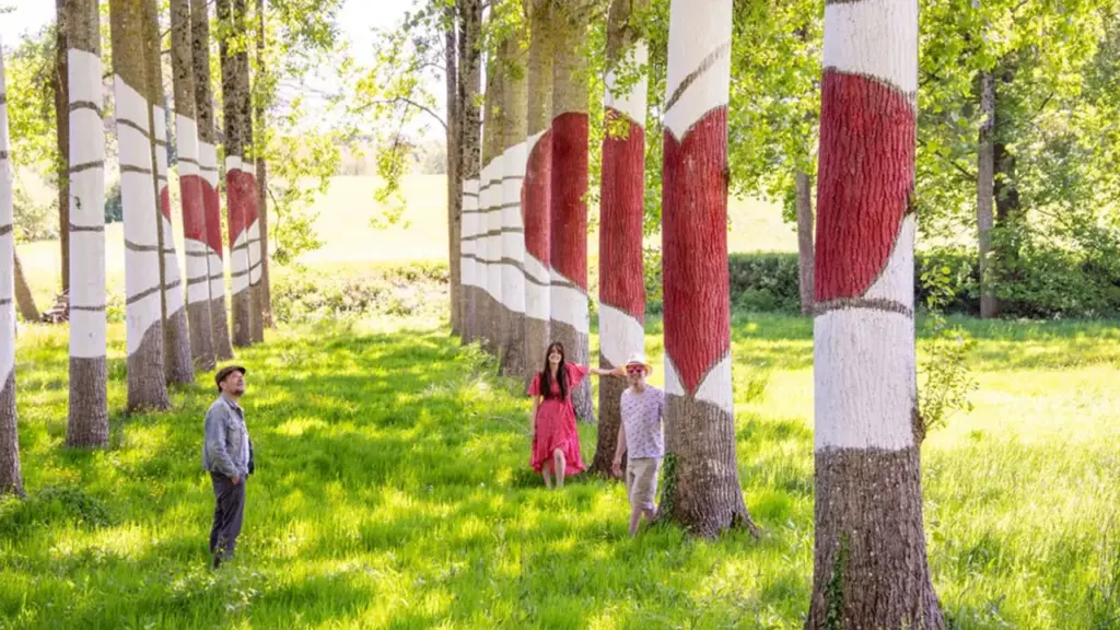 Trois personnes se promènent dans une allée d'arbres peints avec des motifs rouges et blancs.