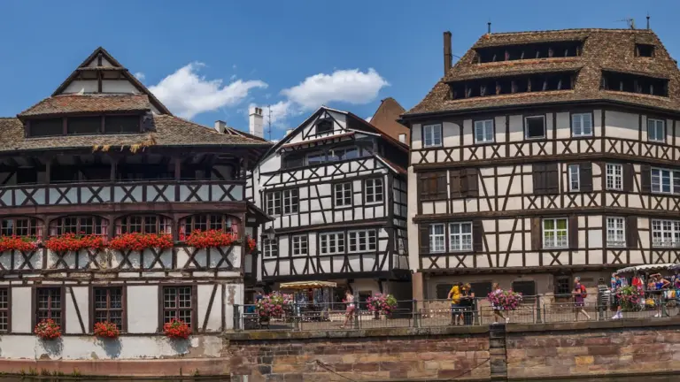 Maisons à colombages traditionnelles le long d'un canal à Mulhouse sous un ciel ensoleillé.