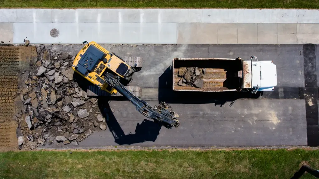 Vue aérienne d'une pelleteuse jaune retirant le bitume d'une route en travaux.