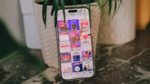 Un téléphone portable affichant des réseaux sociaux posé sur une table près d'une plante.