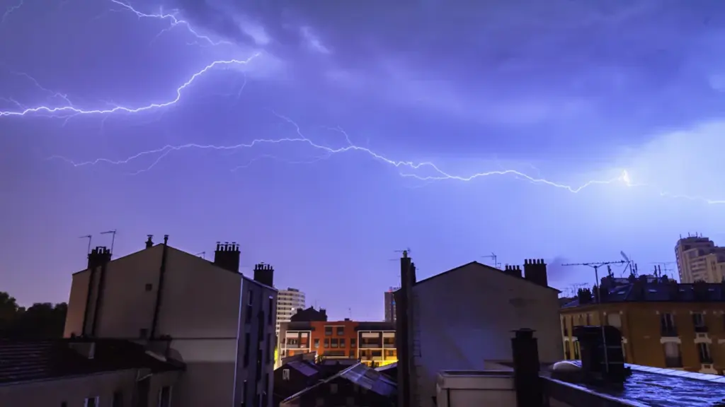 Éclair frappant le ciel au-dessus de bâtiments résidentiels typiquement européens la nuit.