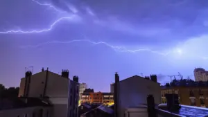 Éclair frappant le ciel au-dessus de bâtiments résidentiels typiquement européens la nuit.