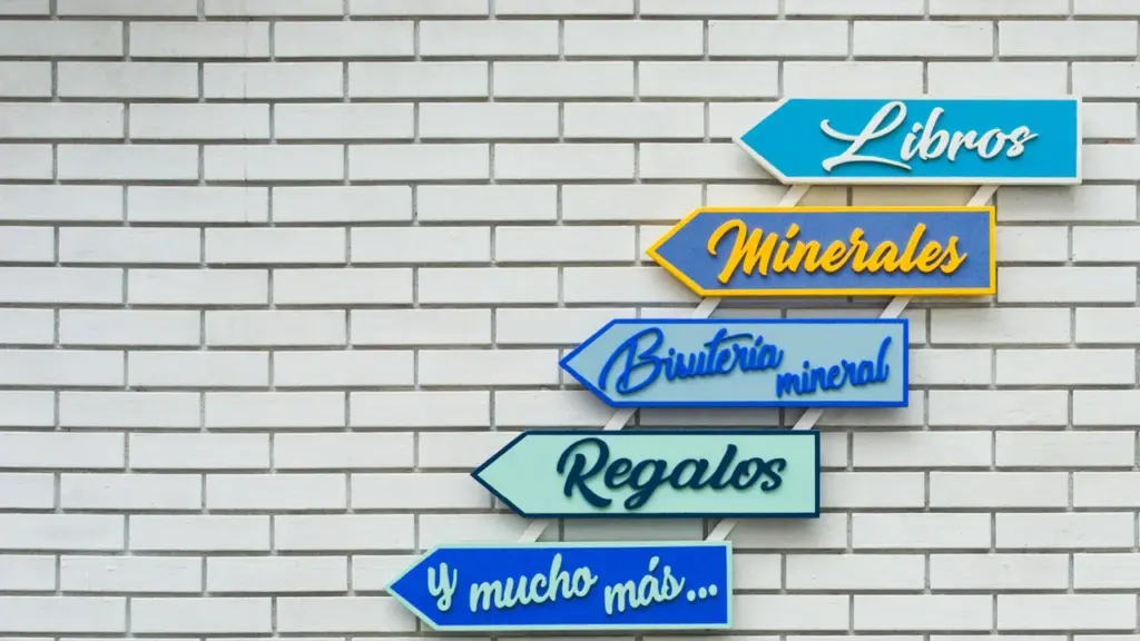 Panneaux directionnels colorés sur un mur en briques indiquant livres et cadeaux.