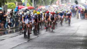Peloton de cyclistes professionnels roulant sur une route mouillée sous la pluie battante.