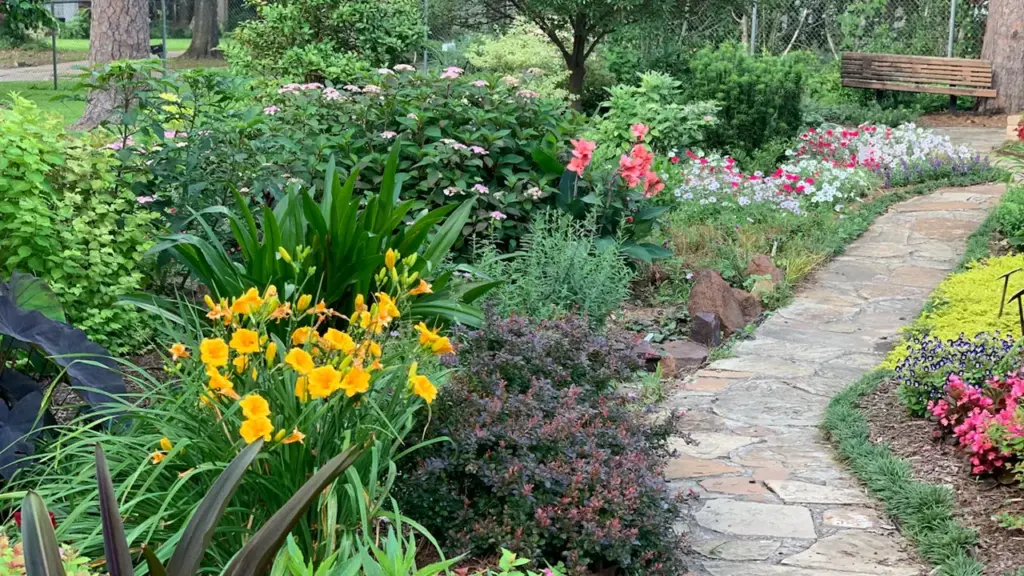 Allée de jardin en pierre bordée de fleurs colorées et de verdure luxuriante.